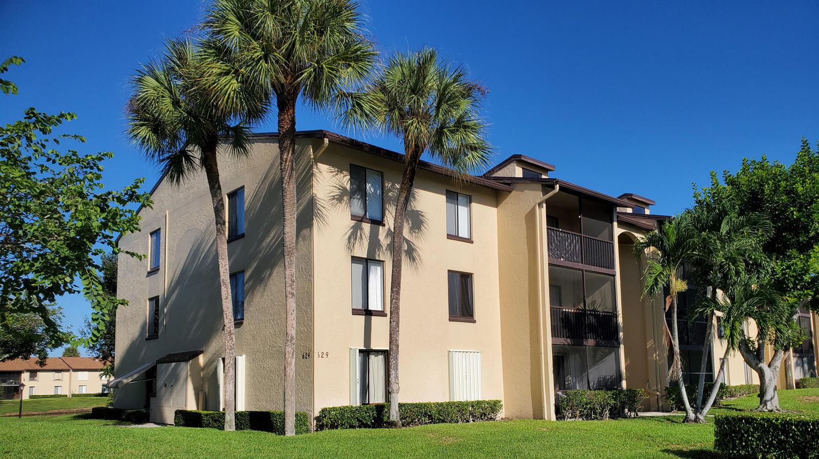 A three-story apartment building with tan stucco walls, screened balconies, and palm trees in front — 629 Sea Pine Way # H3, FL 33415, FL