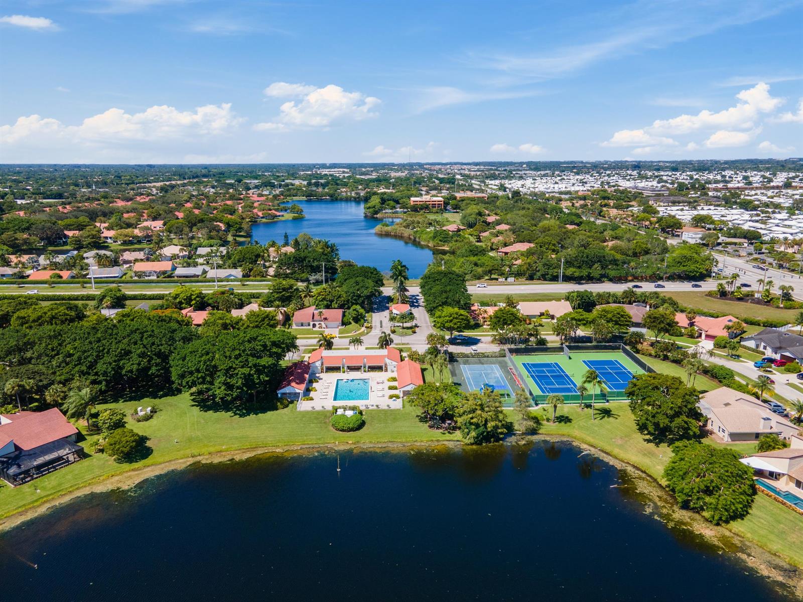 An aerial view shows a community clubhouse with a pool and tennis courts by a lake — 2657 SW 23rd Cranbrook Drive, Boynton Beach FL 33436, BOYNTON BEACH, FL