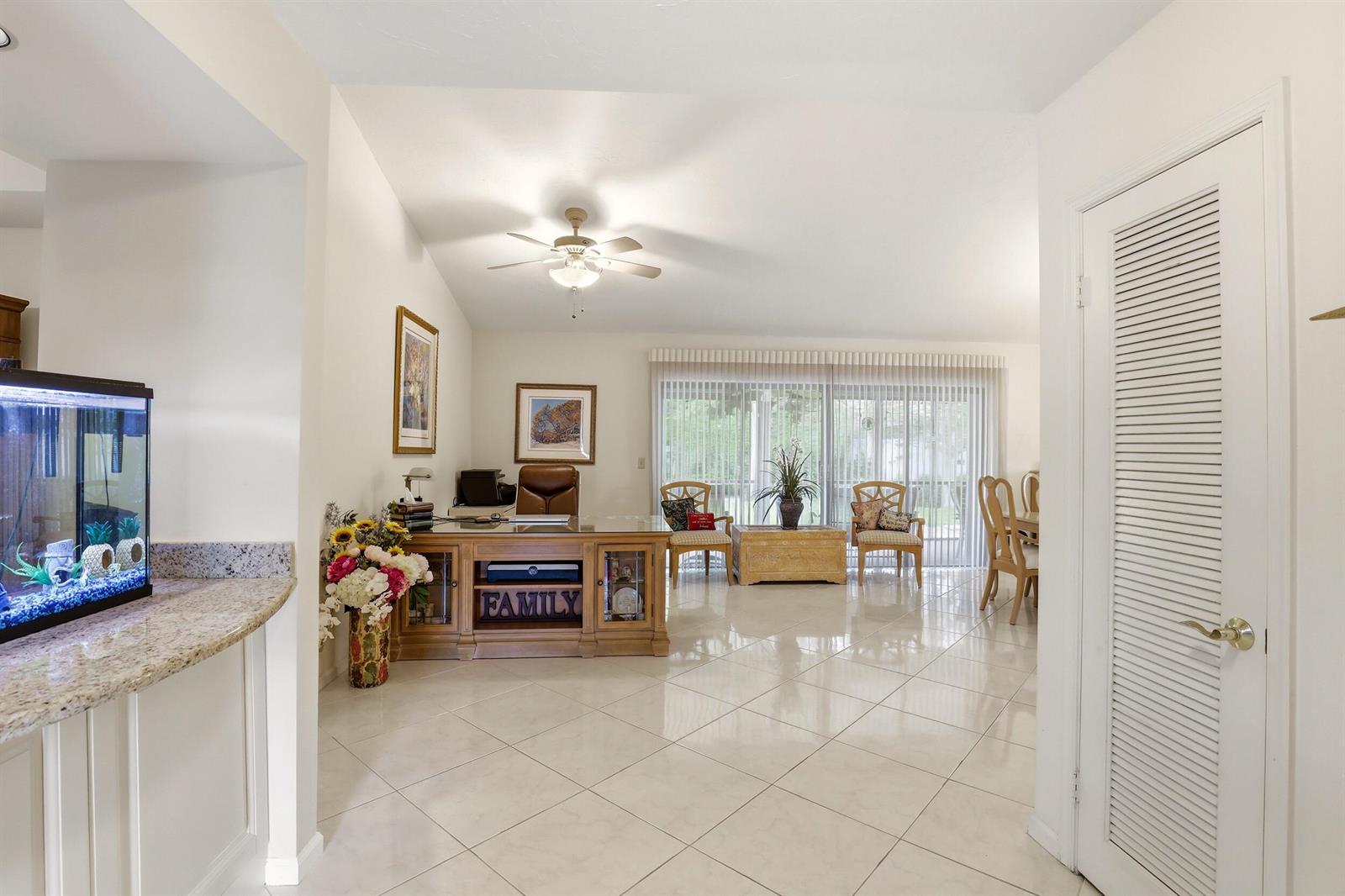 A bright, open-concept room features tile flooring, a wooden desk, and a sliding glass door — 2657 SW 23rd Cranbrook Drive, Boynton Beach FL 33436, BOYNTON BEACH, FL