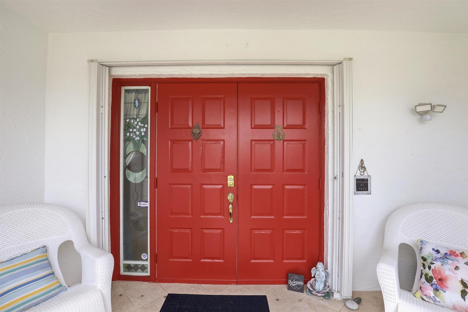 A red double front door with a stained glass sidelight sits between two white chairs — 2657 SW 23rd Cranbrook Drive, Boynton Beach FL 33436, BOYNTON BEACH, FL