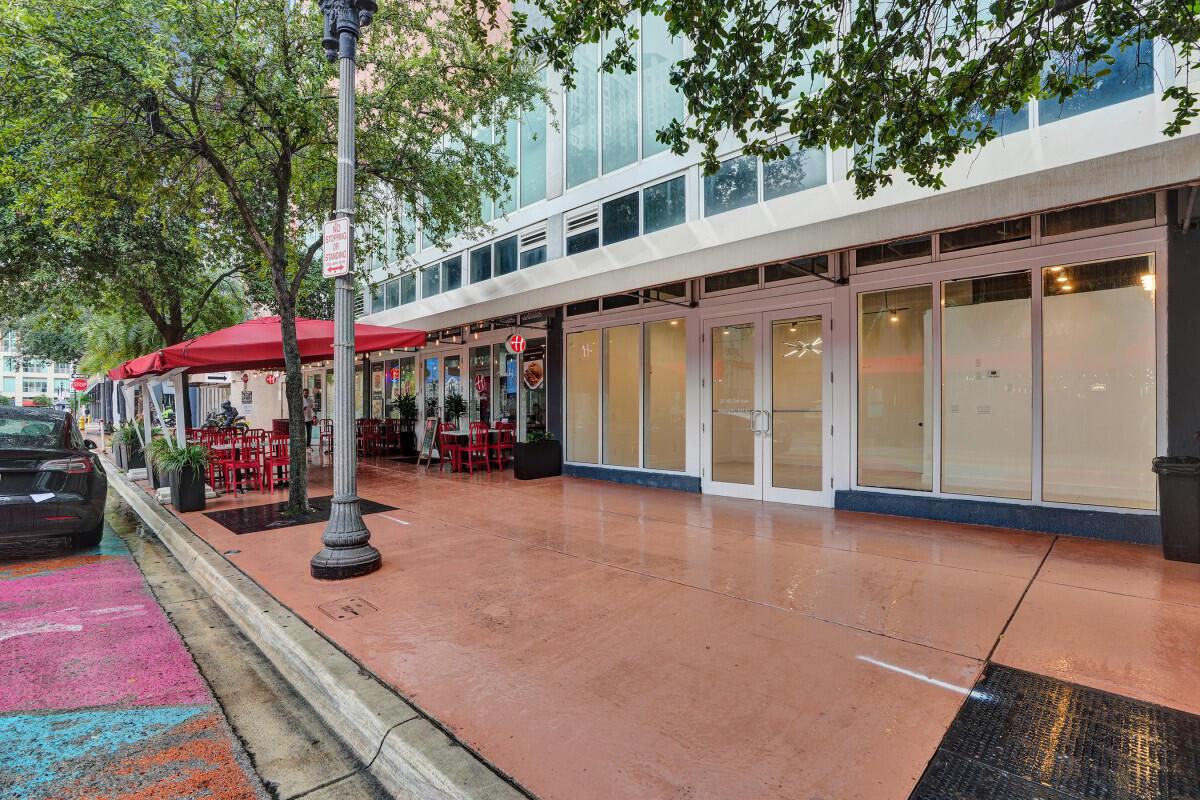 A street-level view of a commercial building exterior with a red awning and outdoor seating — 50 Biscayne Boulevard, Miami FL 33132, MIAMI, FL