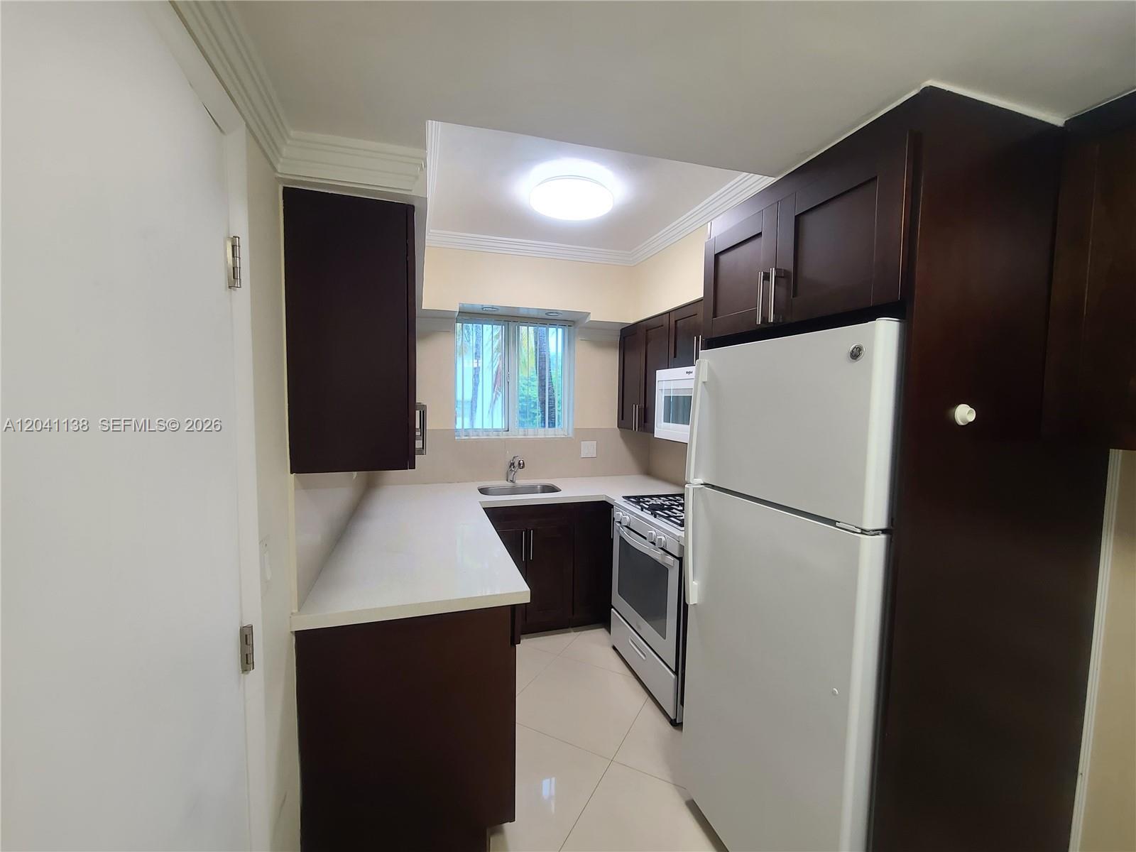 A kitchen features dark wood cabinets, white countertops, a white refrigerator, and tile flooring — 220 Collins Ave # 3B, Miami Beach FL 33139, MIAMI BEACH, FL