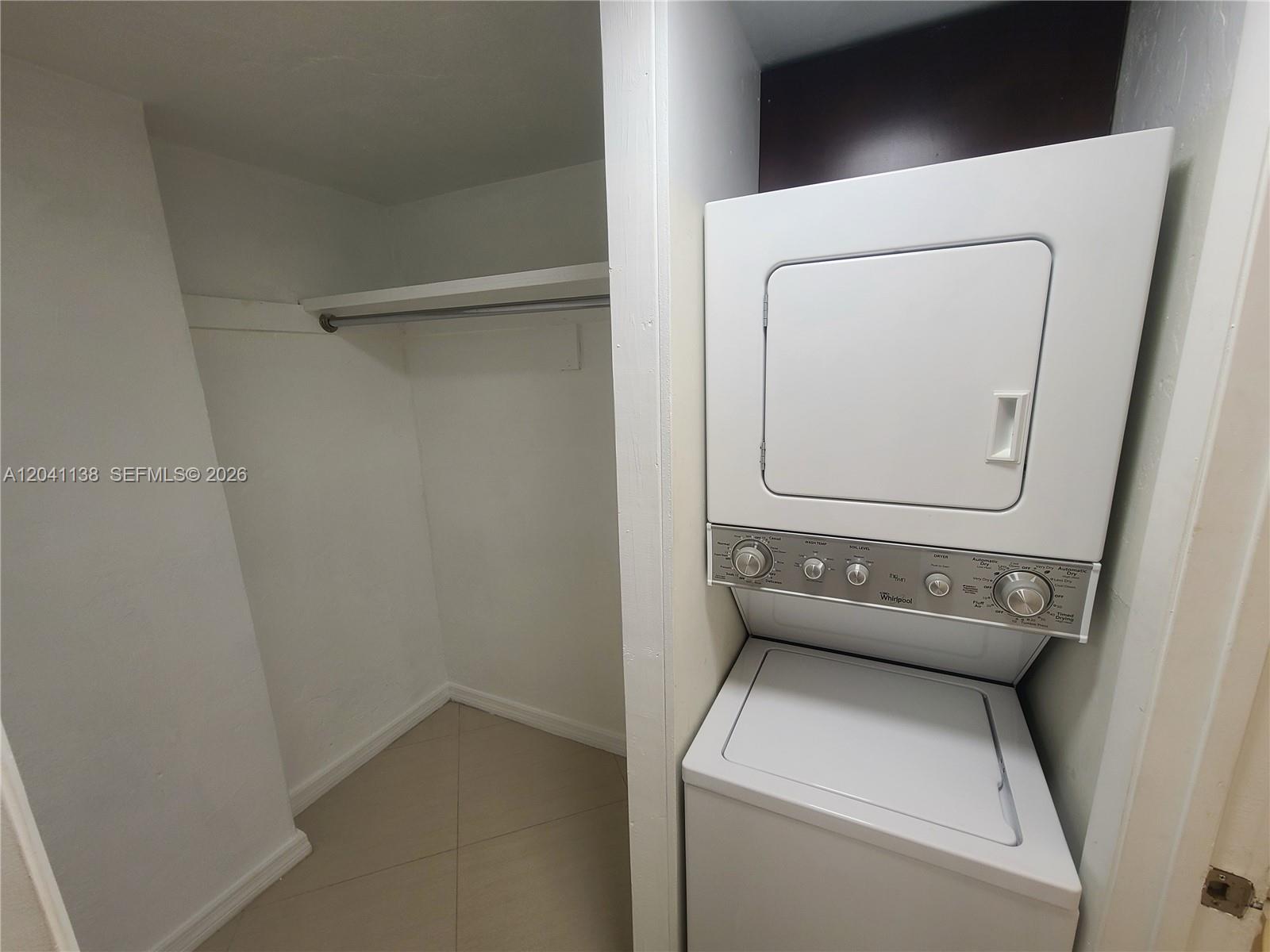 A white stacked washer and dryer unit sits next to an empty closet with shelving — 220 Collins Ave # 3B, Miami Beach FL 33139, MIAMI BEACH, FL