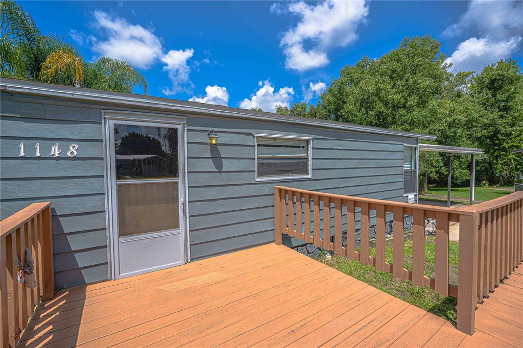 A wooden deck with railings leads to the entrance of a gray-sided mobile home — 1148 MARY FRANCES DRIVE, KISSIMMEE, FL