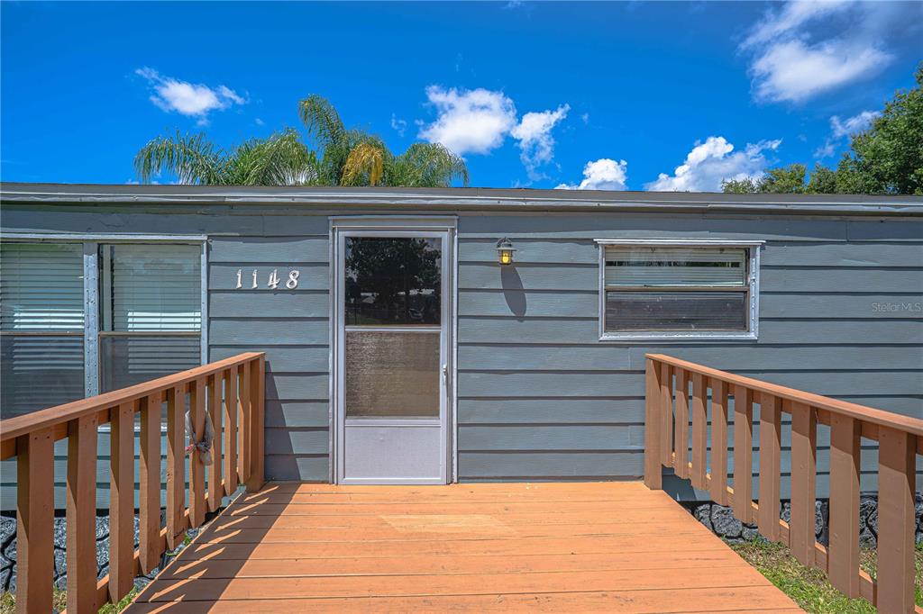 A wooden deck leads to the front entrance of a grey house with horizontal siding — 1148 MARY FRANCES DRIVE, KISSIMMEE, FL