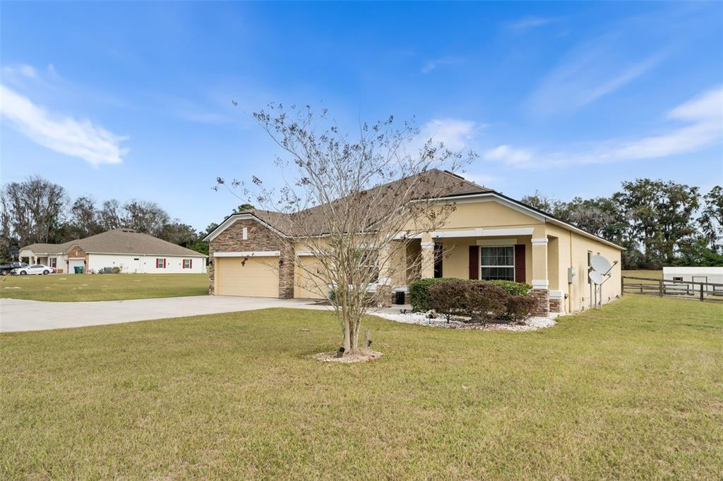 A single-story house with a tan stucco exterior, stone accents, and a concrete driveway — 5615 SW 215TH TERRACE, NEWBERRY, FL