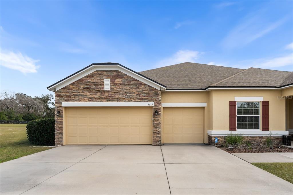 The exterior of a house features a three-car garage, stone accents, and a beige facade — 5615 SW 215TH TERRACE, NEWBERRY, FL