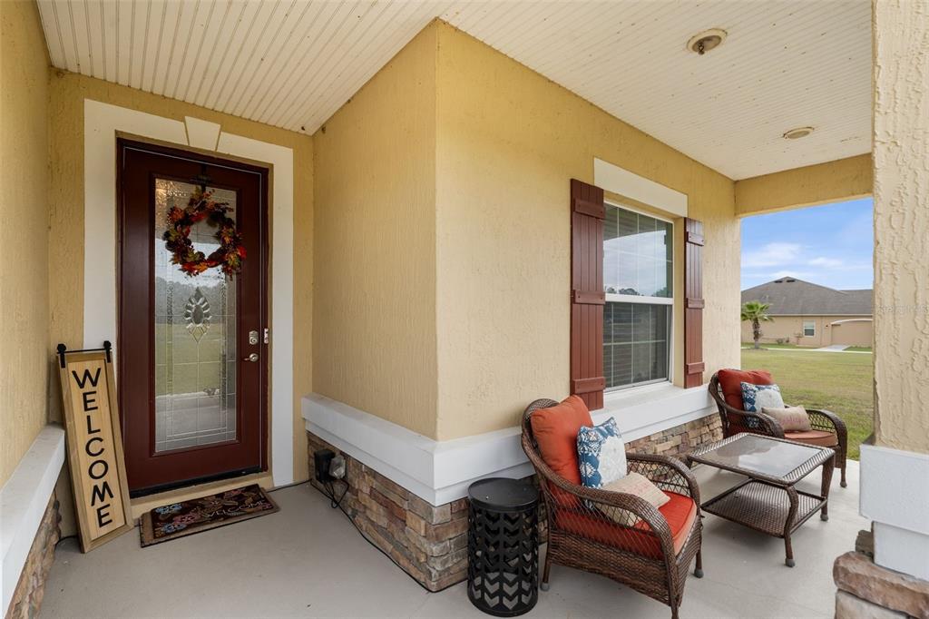 A covered front porch features a brown front door, two wicker chairs, and stone accents — 5615 SW 215TH TERRACE, NEWBERRY, FL