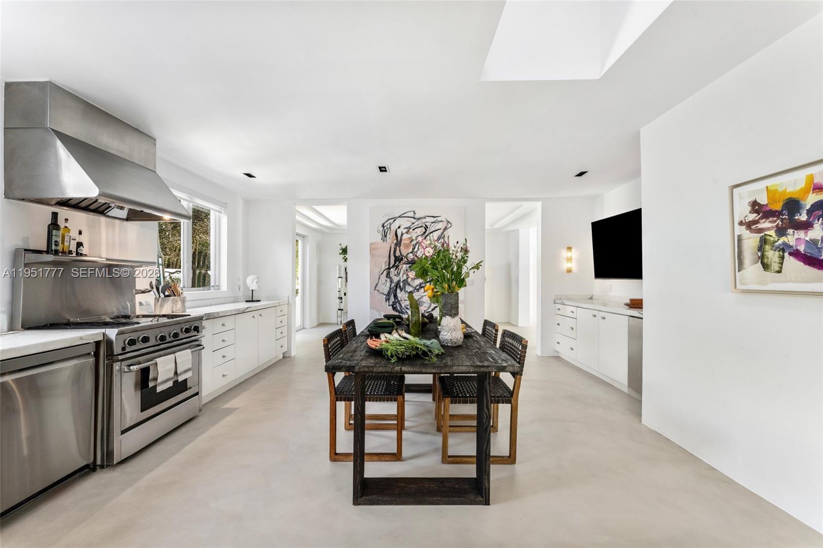 A modern kitchen features white cabinetry, stainless steel appliances, and a dark wooden dining table — 3325 Pine Tree Dr, Miami Beach FL 33140, MIAMI BEACH, FL