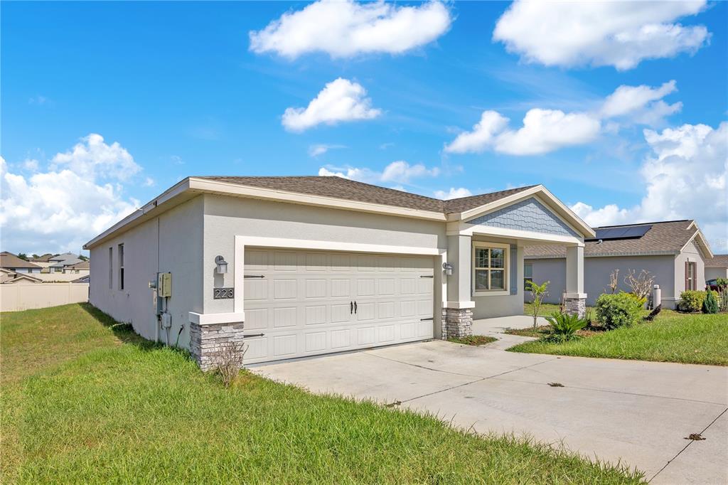 A single-story house with a beige stucco exterior, a two-car garage, and a concrete driveway — 223 BERGAMOT LOOP, DAVENPORT, FL