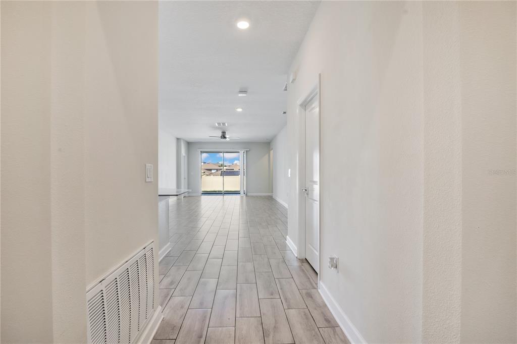 A hallway with light wood-look tile flooring leads to an open living area with sliding doors — 223 BERGAMOT LOOP, DAVENPORT, FL