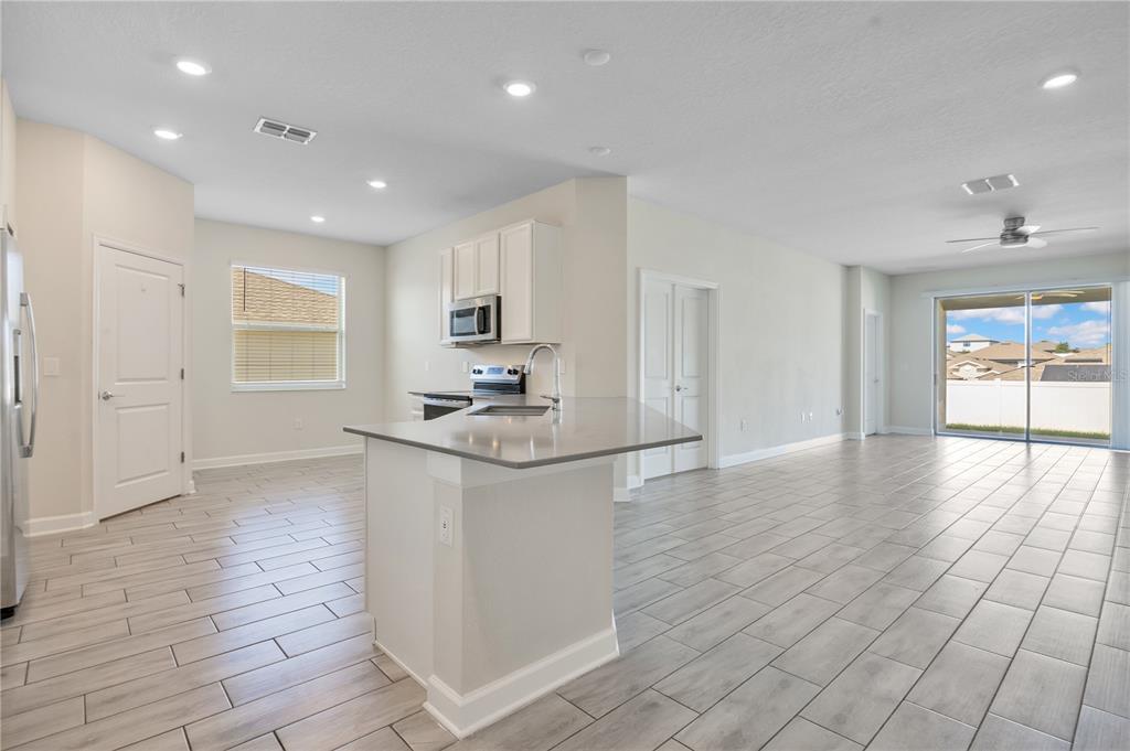 An open-concept kitchen and living area features light-colored tile flooring and a central island — 223 BERGAMOT LOOP, DAVENPORT, FL