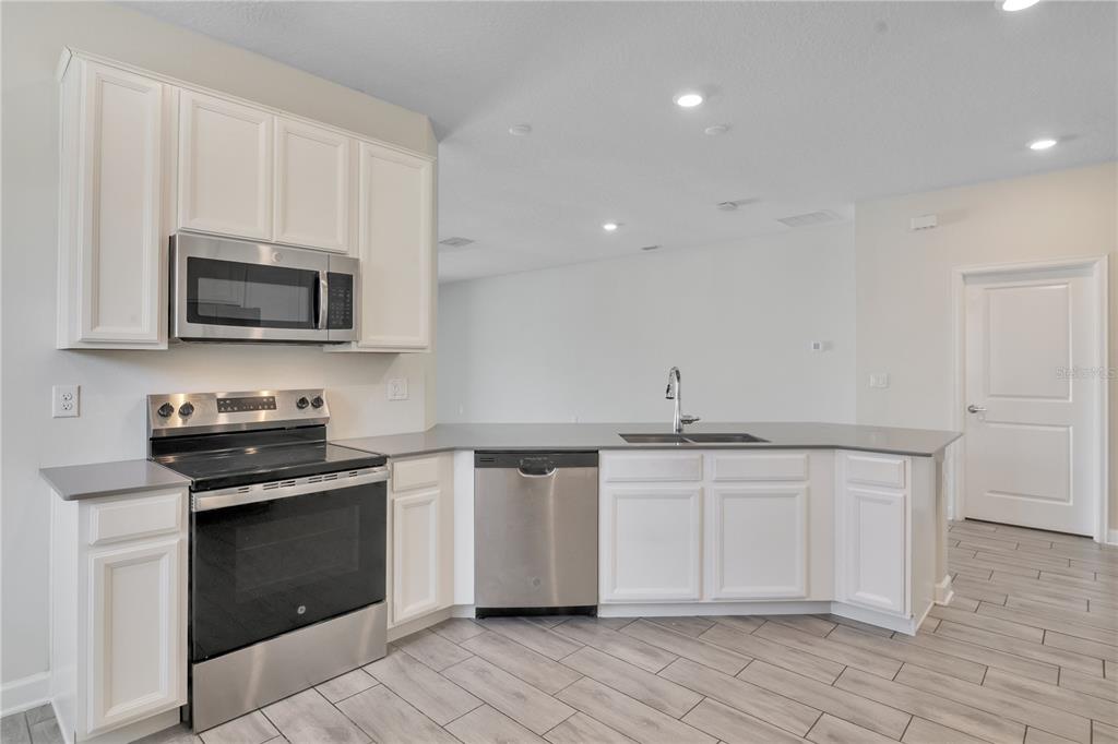 A kitchen features white cabinets, stainless steel appliances, gray countertops, and light wood-look tile flooring — 223 BERGAMOT LOOP, DAVENPORT, FL