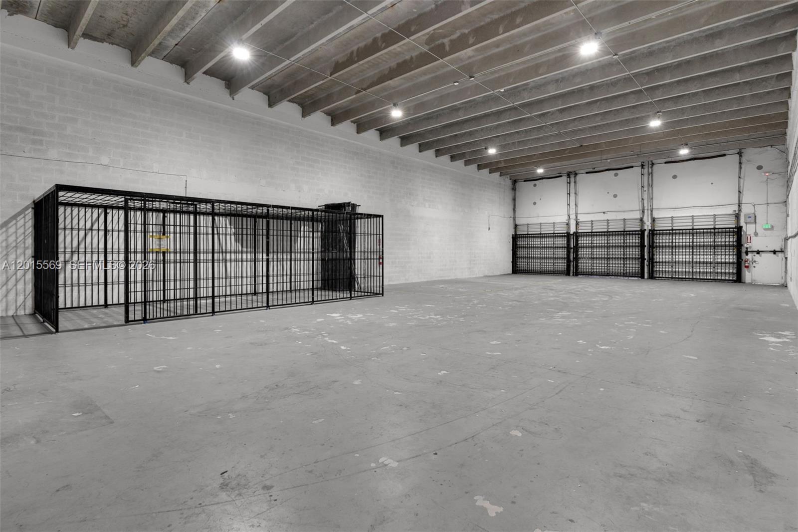 An industrial warehouse space features concrete walls, an exposed ceiling, and metal security cages — 8216 NW 30th Ter, Doral FL 33122, DORAL, FL