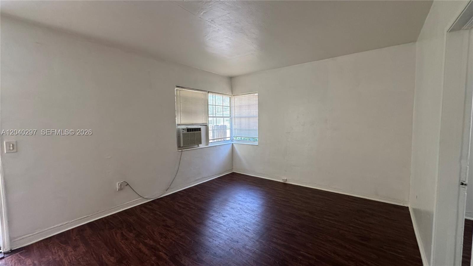 An empty room features white walls, dark wood-look flooring, and a corner window with blinds — 4410 NE 2nd Ave # 4410, Miami FL 33137, MIAMI, FL