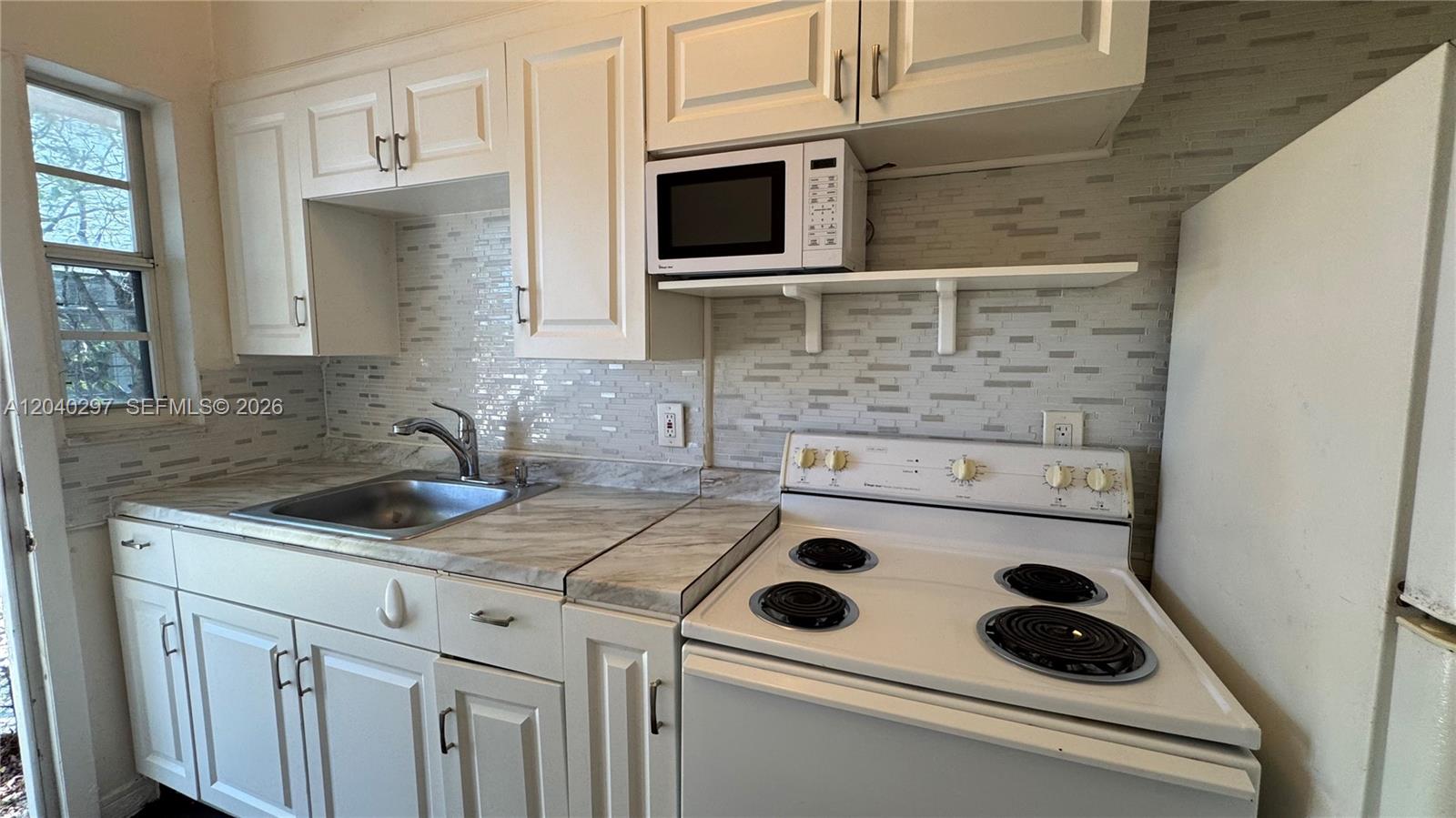 A kitchen features white cabinets, a marble-patterned countertop, a stainless steel sink, and white appliances — 4410 NE 2nd Ave # 4410, Miami FL 33137, MIAMI, FL