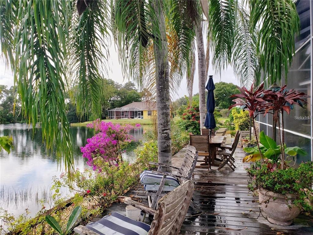 A wooden deck overlooks a lake with palm trees, patio furniture, and a distant house — 5125 MAGNOLIA POND DRIVE, SARASOTA, FL