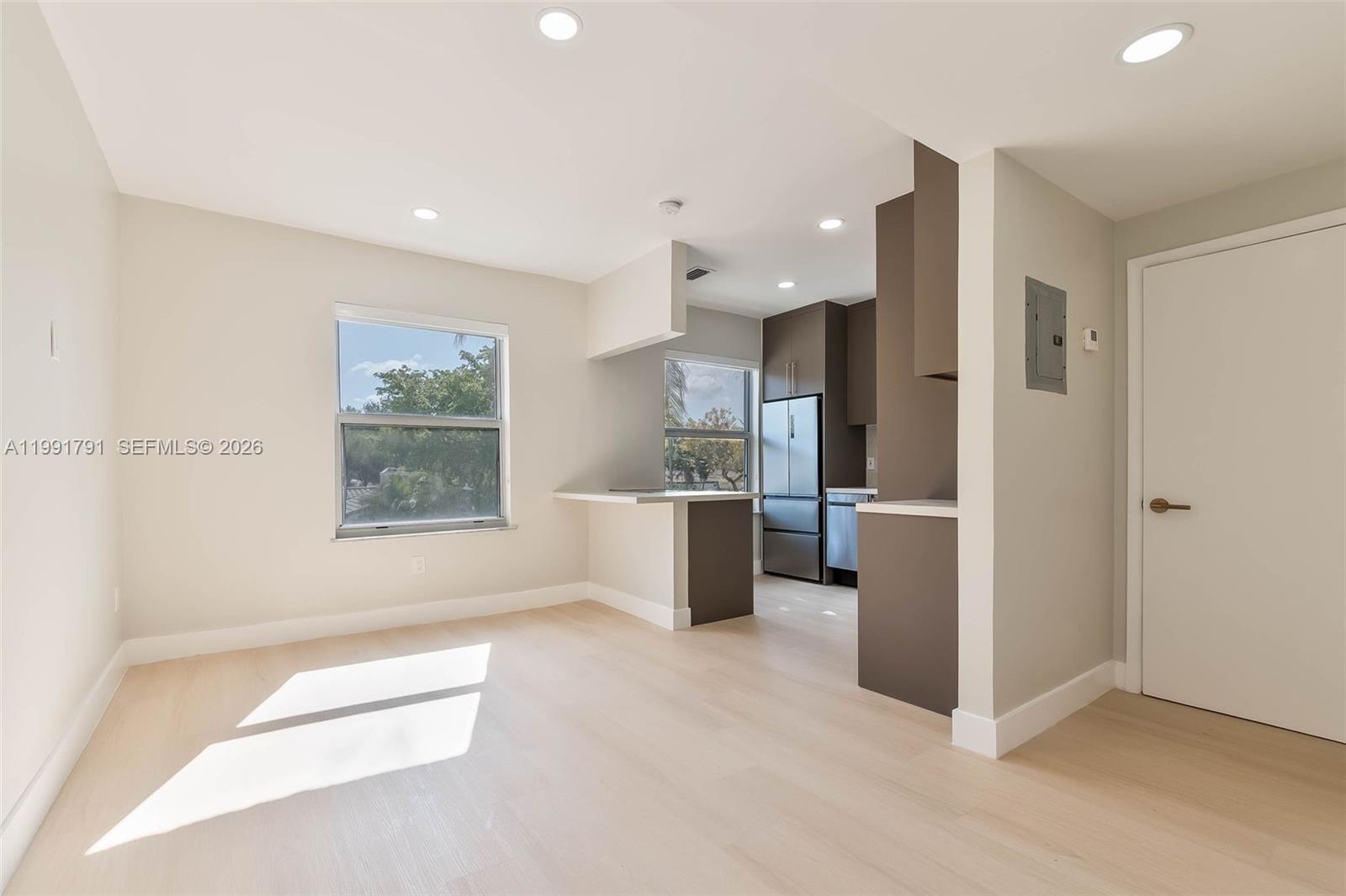This room features light wood flooring, recessed lighting, and an open kitchen with dark cabinetry — 694 NE 76th St # 6, Miami FL 33138, MIAMI, FL