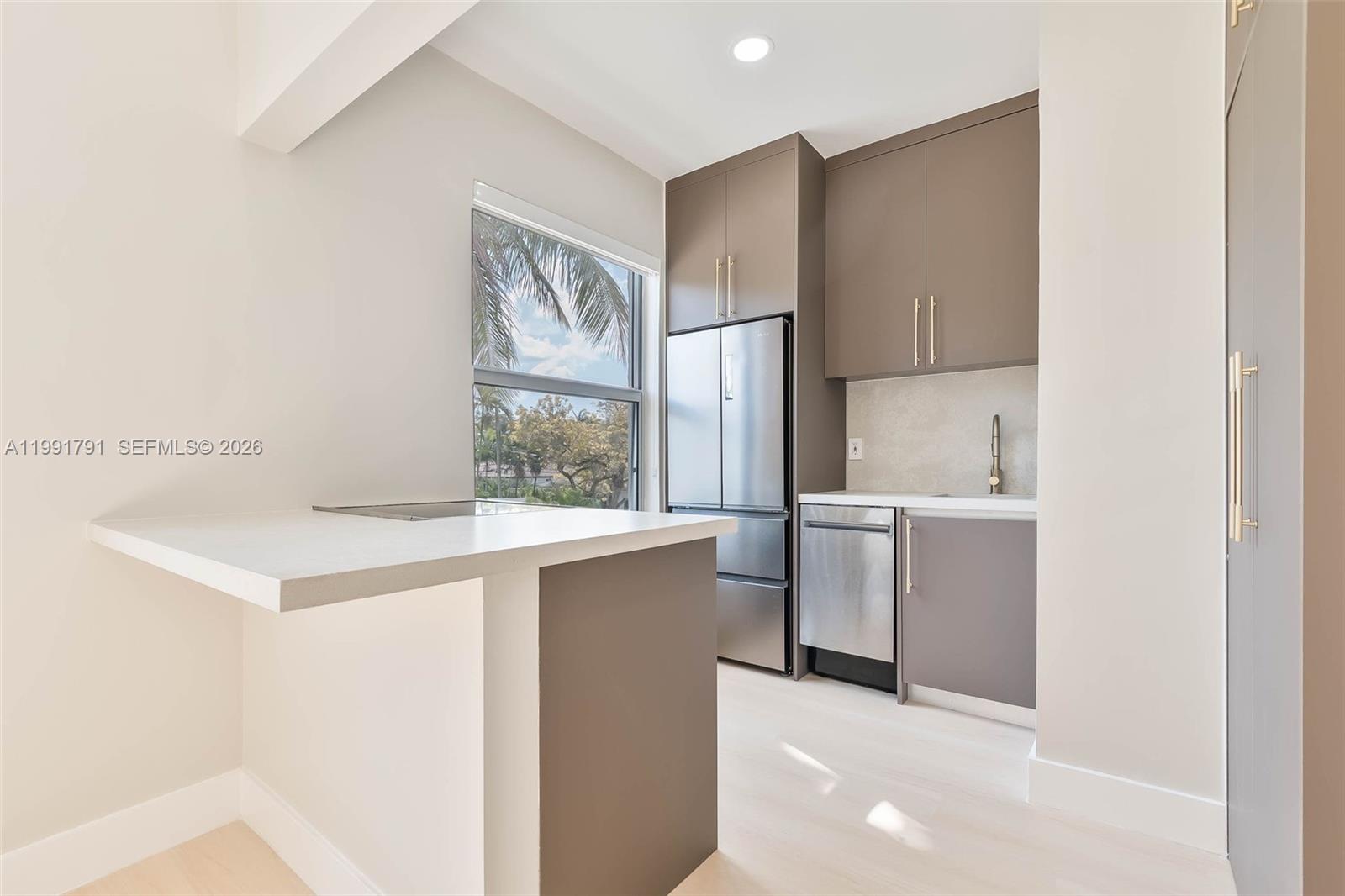 A modern kitchen features taupe cabinets, stainless steel appliances, and a white breakfast bar — 694 NE 76th St # 6, Miami FL 33138, MIAMI, FL