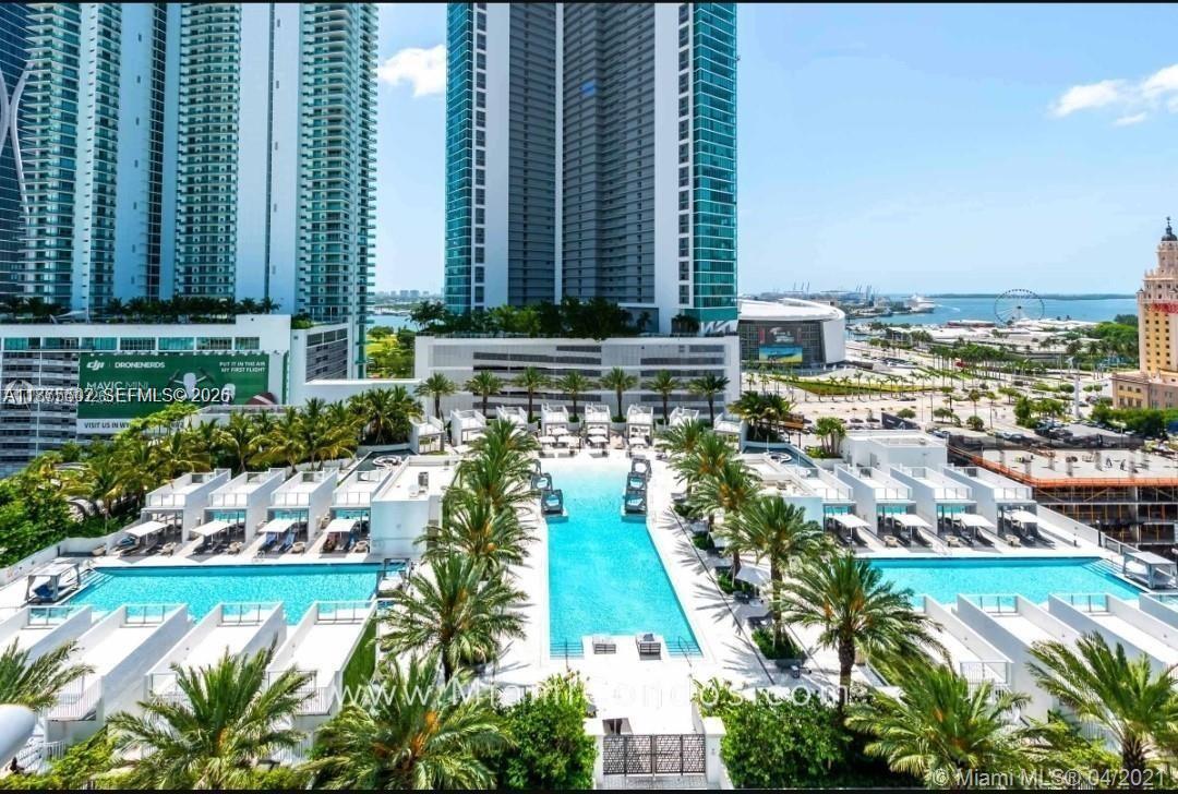 An aerial view shows a large swimming pool surrounded by palm trees and modern residential buildings — 851 NE 1st Ave # 1203, Miami FL 33132, MIAMI, FL