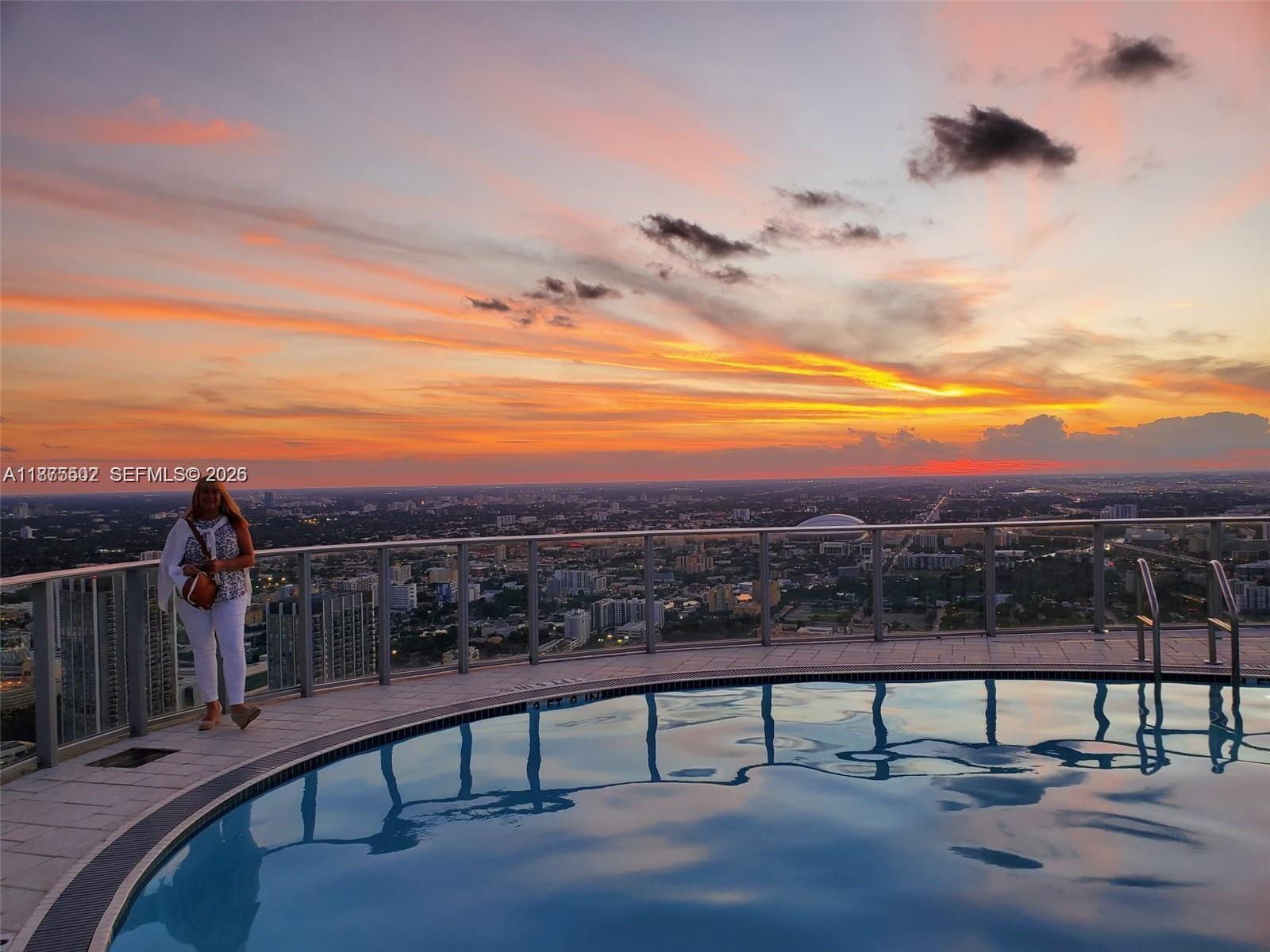 A woman stands on a high-rise balcony next to a circular pool overlooking a city — 851 NE 1st Ave # 1203, Miami FL 33132, MIAMI, FL