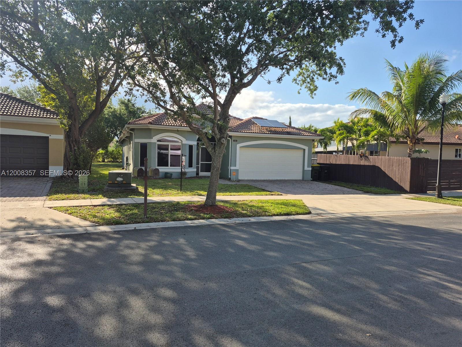 A single-story house with a two-car garage, tile roof, and a large tree in front — 161 SE 22nd Ter, Homestead FL 33033, HOMESTEAD, FL