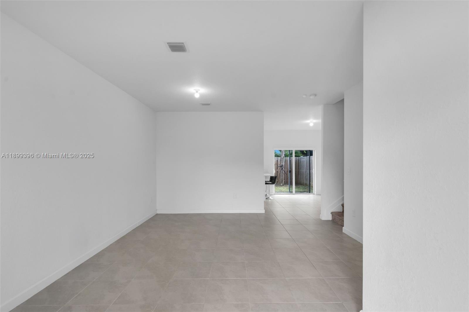 An empty room with light tile flooring leads to a sliding glass door and patio — 12523 NW 24th Ave, Miami FL 33167, MIAMI, FL
