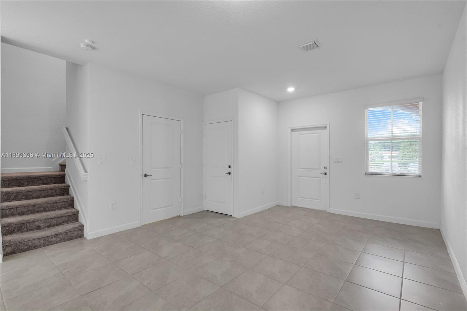 An empty room features tile flooring, a carpeted staircase, three white doors, and a window — 12523 NW 24th Ave, Miami FL 33167, MIAMI, FL