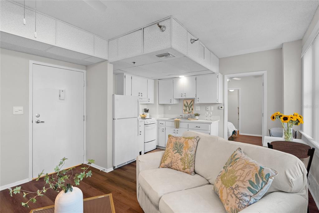 A small kitchen with white cabinets and appliances is open to a living area — 411 1ST AVENUE N UNIT 307, ST PETERSBURG, FL
