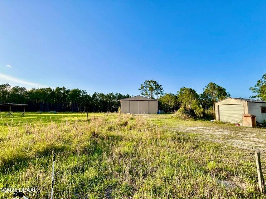 A grassy field features a large metal workshop and a smaller shed under a blue sky — 201 WASICK LANE, ORMOND BEACH, FL