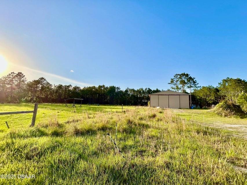 A metal barn stands in a grassy field bordered by a line of trees — 201 WASICK LANE, ORMOND BEACH, FL