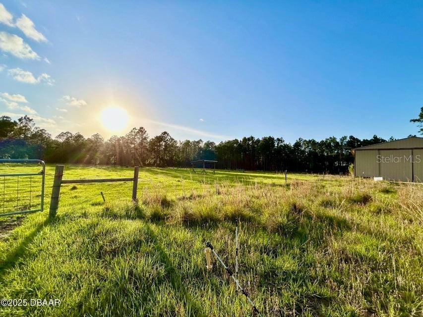 A grassy field features a wire fence, a small wooden structure, and a metal building — 201 WASICK LANE, ORMOND BEACH, FL