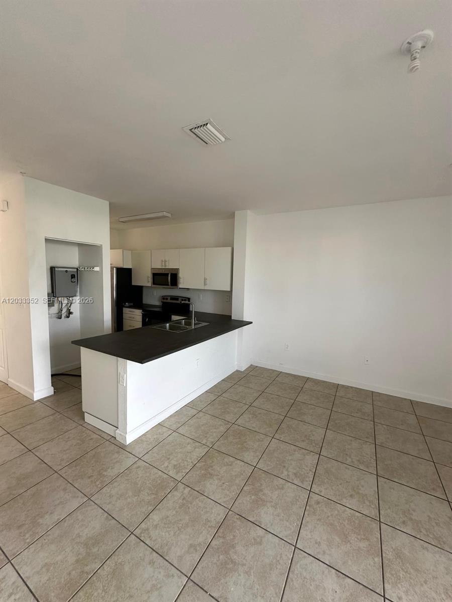 A kitchen with white cabinets and a dark countertop overlooks a tiled living area — 2819 SE 1st Dr # 9, Homestead FL 33033, HOMESTEAD, FL