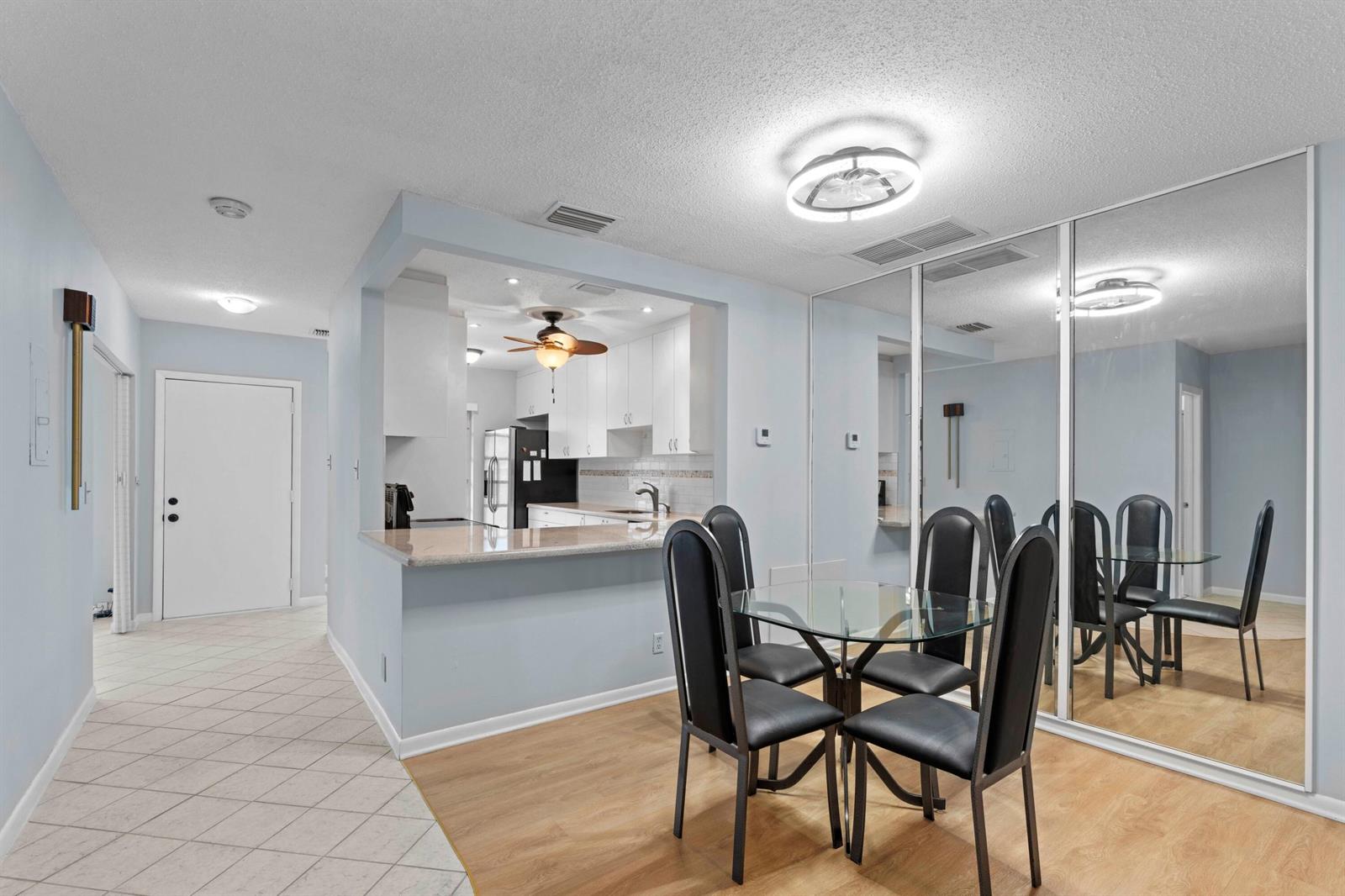 A dining area with a glass table and black chairs sits beside a mirrored wall — 8555 Bella Vista Drive # 86, Boca Raton FL 33433, BOCA RATON, FL