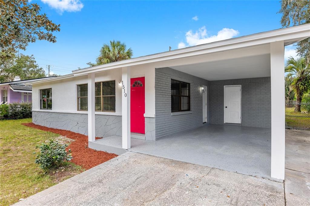 A single-story house features a bright pink front door, gray brick siding, and a carport — 1510 SE 14TH AVENUE, GAINESVILLE, FL