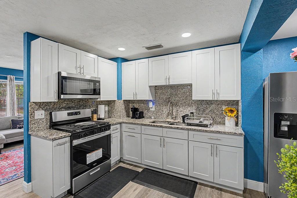 A kitchen features white cabinets, granite countertops, stainless steel appliances, and blue accent walls — 1510 SE 14TH AVENUE, GAINESVILLE, FL