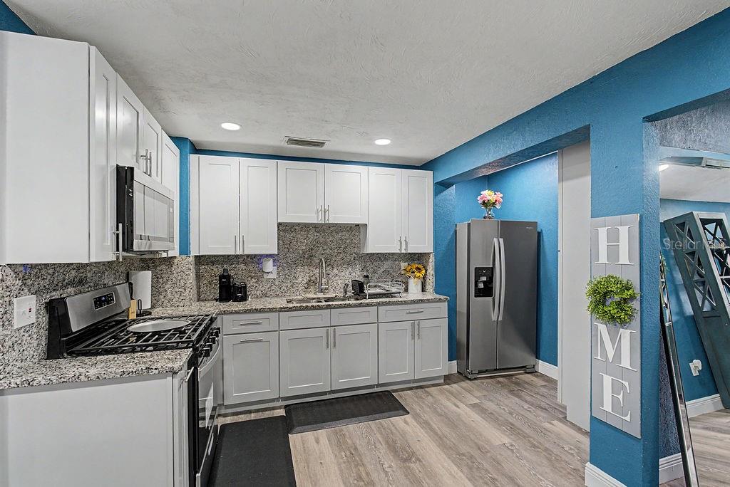 A kitchen features white cabinets, granite countertops, stainless steel appliances, and blue accent walls — 1510 SE 14TH AVENUE, GAINESVILLE, FL