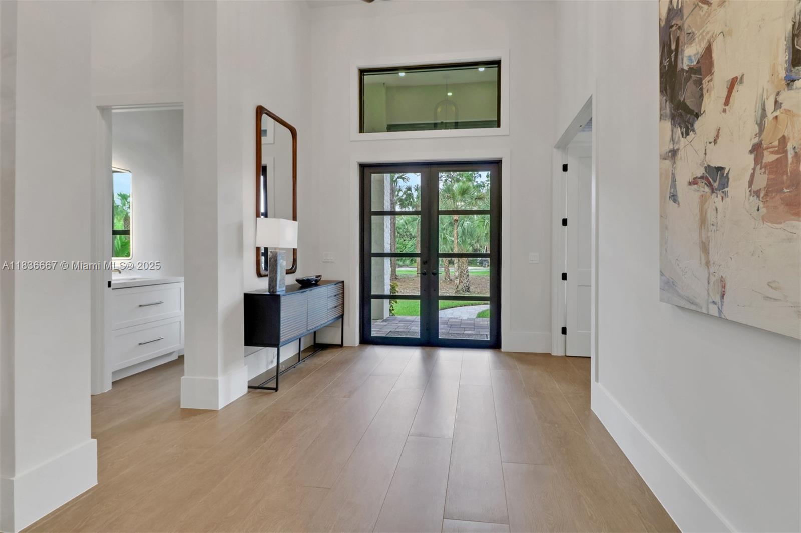A bright entryway features light wood floors, a dark console table, and double glass doors — 524 13th St Sw, Naples FL 34117, NAPLES, FL