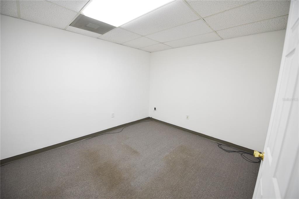 An empty office room features white walls, a drop ceiling, and gray carpeted flooring — 1200 N CENTRAL AVENUE UNIT 210, KISSIMMEE, FL