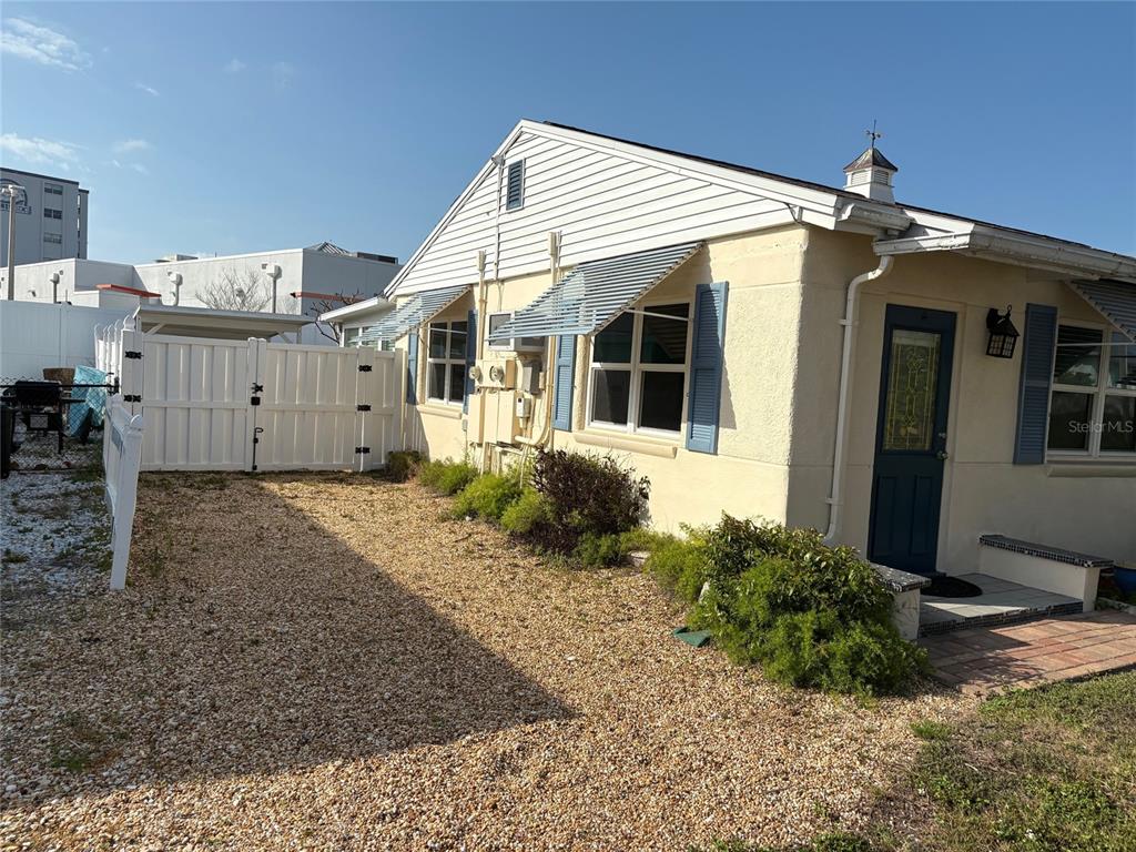 A side view of a one-story house with light-colored siding, blue shutters, and a gravel yard — 111 174TH AVENUE E, REDINGTON SHORES, FL