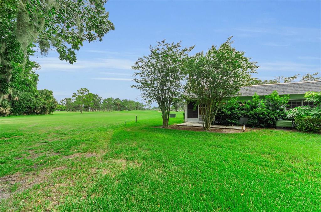 A grassy backyard view of a house exterior with a screened porch and golf course — 3684 TROPHY BOULEVARD, NEW PORT RICHEY, FL