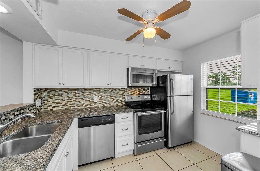 A kitchen features white cabinets, granite countertops, stainless steel appliances, and a mosaic tile backsplash — 3684 TROPHY BOULEVARD, NEW PORT RICHEY, FL