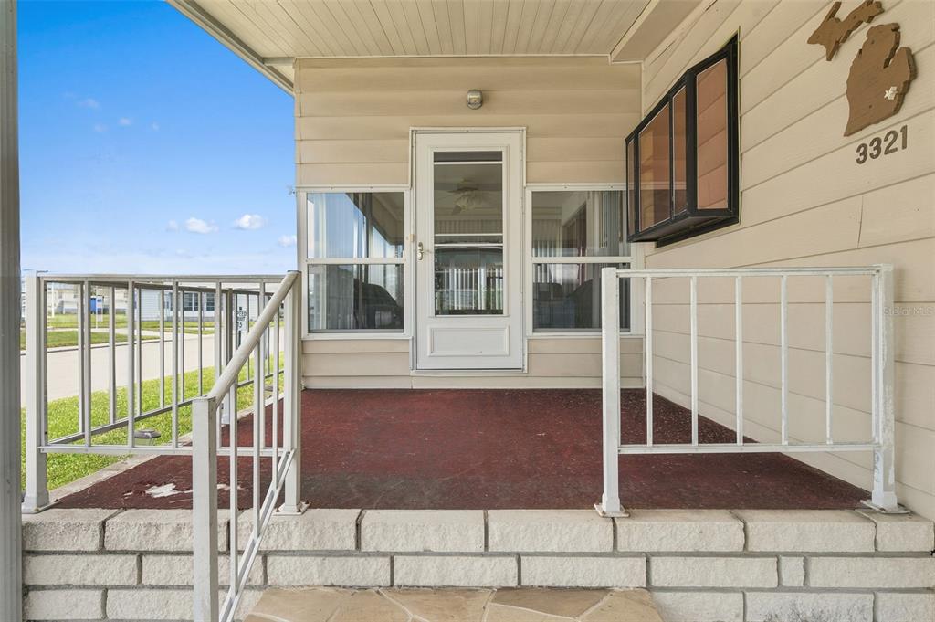 A covered porch with a red floor, white railings, and a glass storm door — 3321 CHATFORD DRIVE, HOLIDAY, FL