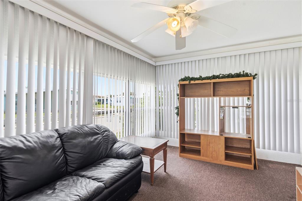 A living room features a black leather sofa, a wooden shelf unit, and vertical blinds — 3321 CHATFORD DRIVE, HOLIDAY, FL