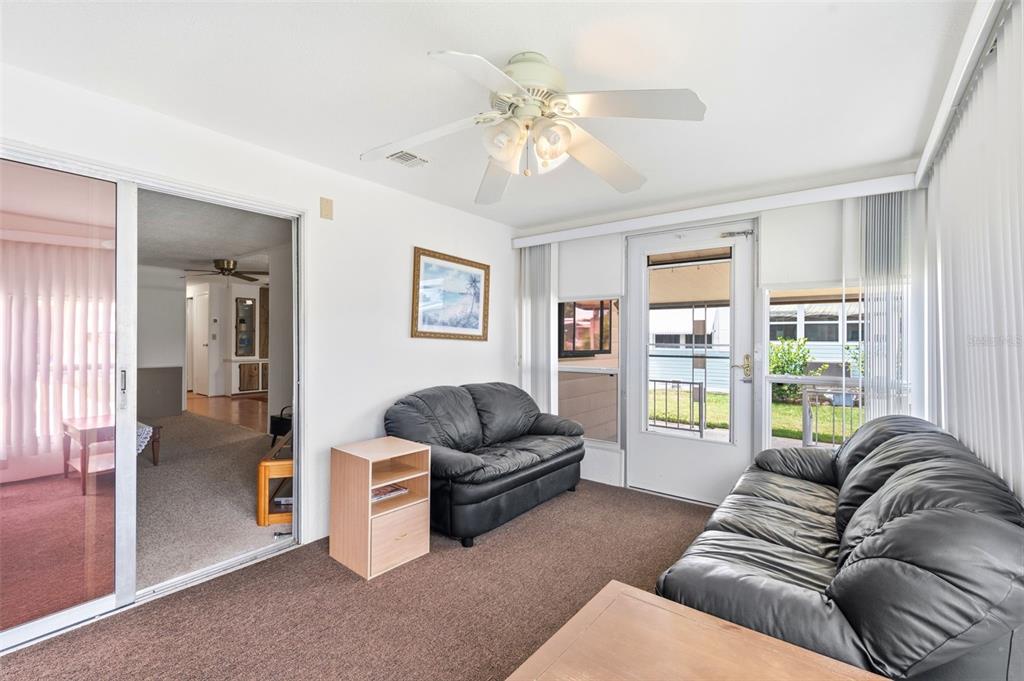 A sunroom features brown carpeting, two black leather sofas, a ceiling fan, and a sliding glass door — 3321 CHATFORD DRIVE, HOLIDAY, FL