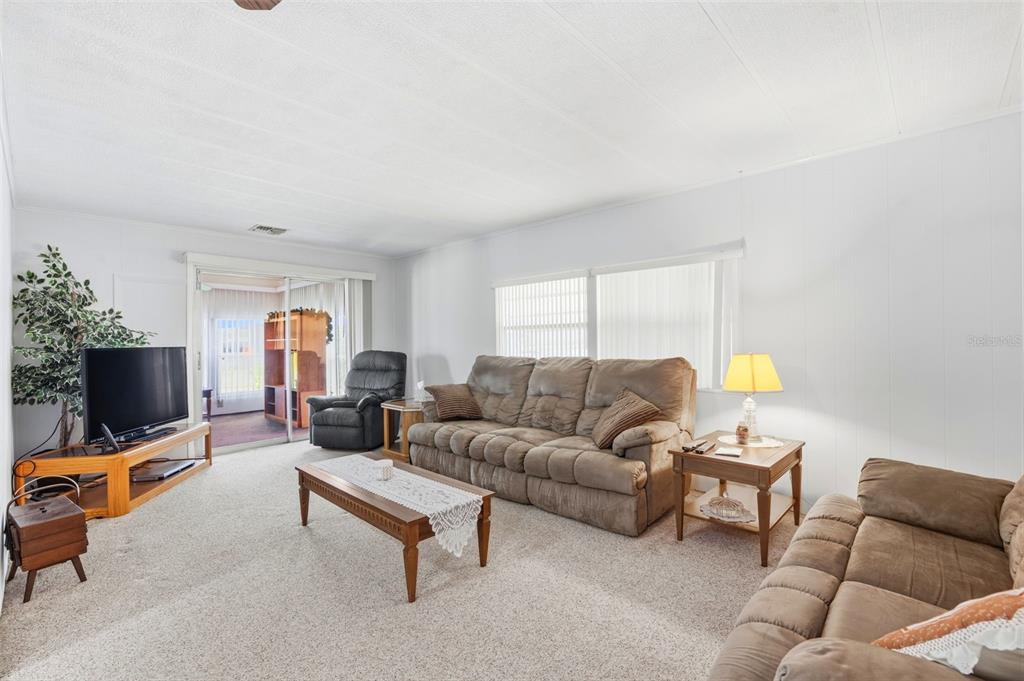 A living room features a brown sofa, a coffee table, and a television on a stand — 3321 CHATFORD DRIVE, HOLIDAY, FL