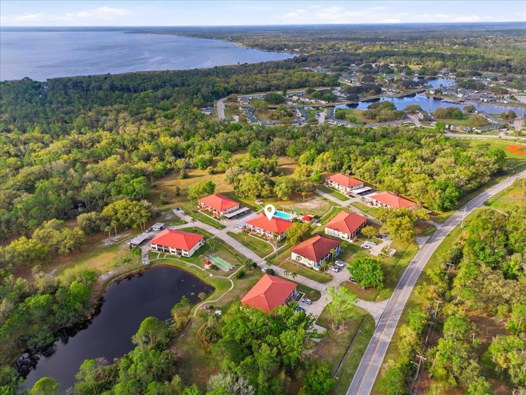 An aerial view shows several buildings with red roofs surrounded by trees and a pond — 2903 GRANADA COURT UNIT 2903, LAKE WALES, FL