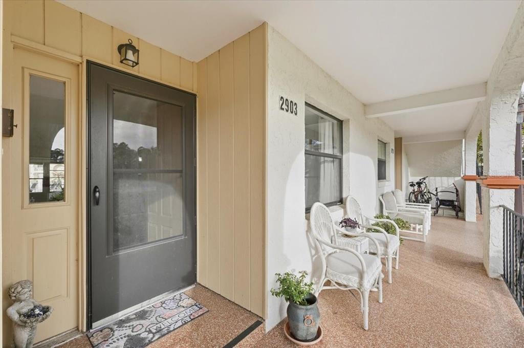 A covered porch features white wicker chairs, a dark front door, and a potted plant — 2903 GRANADA COURT UNIT 2903, LAKE WALES, FL
