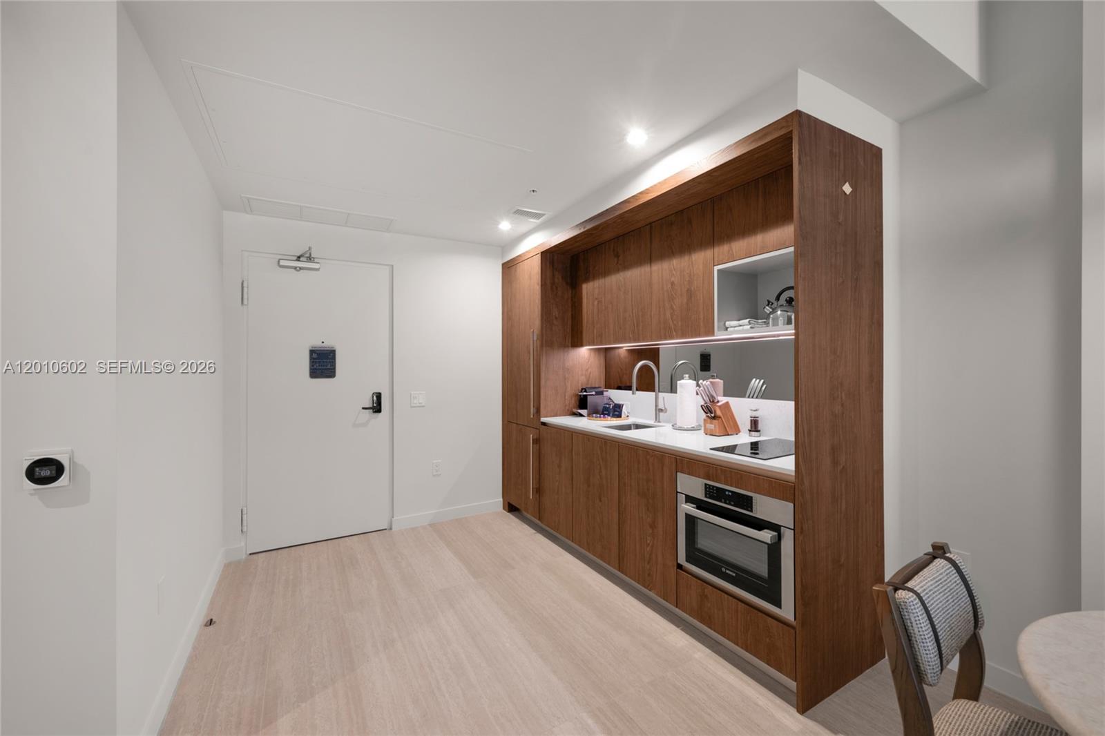 A modern kitchenette with wood cabinetry and white countertops is situated next to an entryway door — 1611 SW 2nd Ave # 414, Miami FL 33129, MIAMI, FL