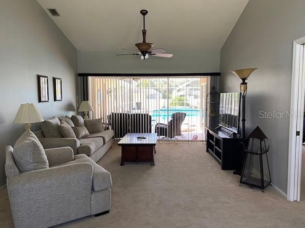 A living room with a vaulted ceiling, beige carpet, and sliding glass doors overlooking a pool — 3645 SLAYTON AVENUE, NORTH PORT, FL